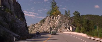 Movie still from “Double Jeopardy” (1999), directed by Bruce Beresford – A car driving down a road next to a rock wall; Extreme Wide shot, Low angle