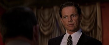 Movie still from “Double Jeopardy” (1999), directed by Bruce Beresford – A man in a suit and tie standing in front of a curtain; Close Up shot, Over the shoulder angle