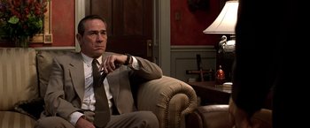 Movie still from “Double Jeopardy” (1999), directed by Bruce Beresford – A man sitting on a couch wearing a suit and tie; Medium shot, Low angle