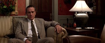 Movie still from “Double Jeopardy” (1999), directed by Bruce Beresford – A man in a suit and tie sitting on a couch; Medium shot, Low angle