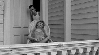 Movie still from “Down by Law” (1986), directed by Jim Jarmusch – A woman sitting in a chair next to a man on a porch; Medium shot, Low angle