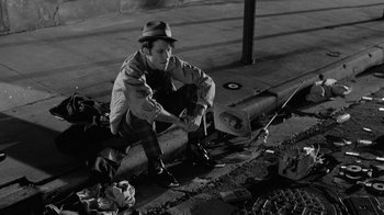 Movie still from “Down by Law” (1986), directed by Jim Jarmusch – A man sitting on the side of a road; Wide shot, High angle