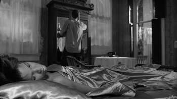 Movie still from “Down by Law” (1986), directed by Jim Jarmusch – A man standing in front of a mirror in front of a bed; Medium shot, Over the shoulder angle