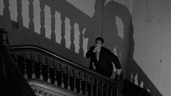 Movie still from “Down by Law” (1986), directed by Jim Jarmusch – A black and white photo of a man standing on the stairs; Wide shot, Low angle