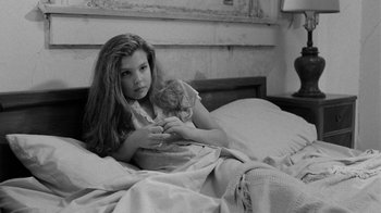 Movie still from “Down by Law” (1986), directed by Jim Jarmusch – A young girl holding a teddy bear while laying in bed; Medium shot, High angle