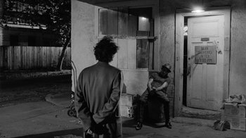 Movie still from “Down by Law” (1986), directed by Jim Jarmusch – Two men are sitting on the porch of a building; Wide shot, Over the shoulder angle