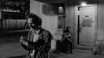 Movie still from “Down by Law” (1986), directed by Jim Jarmusch – A man standing next to another man sitting on a chair; Medium shot, Over the shoulder angle