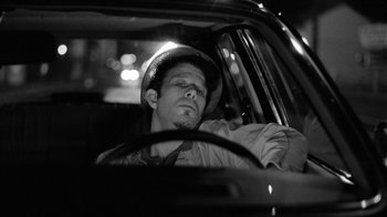 Movie still from “Down by Law” (1986), directed by Jim Jarmusch – A man wearing a helmet sitting in the driver's seat of a car; Close Up shot, Low angle