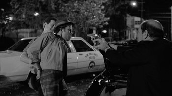 Movie still from “Down by Law” (1986), directed by Jim Jarmusch – A man holding a gun pointed at another man in front of a police car; Medium shot, Over the shoulder angle