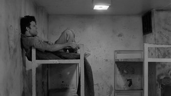 Movie still from “Down by Law” (1986), directed by Jim Jarmusch – A person laying on top of a bunk bed in a room; Wide shot, High angle