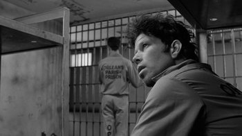 Movie still from “Down by Law” (1986), directed by Jim Jarmusch – A man sitting in front of a jail cell with another man standing behind him; Close Up shot, Over the shoulder angle