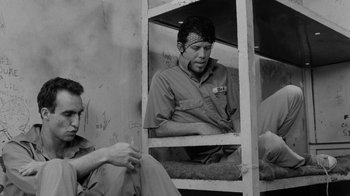 Movie still from “Down by Law” (1986), directed by Jim Jarmusch – A man sitting in a chair next to another man; Medium shot, Low angle