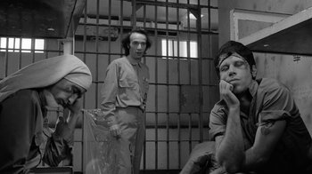 Movie still from “Down by Law” (1986), directed by Jim Jarmusch – A group of people sitting in front of a jail cell; Medium shot, Over the shoulder angle