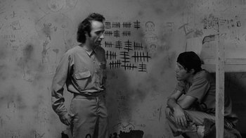 Movie still from “Down by Law” (1986), directed by Jim Jarmusch – A man standing next to a woman in front of a wall; Medium shot, High angle
