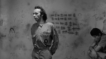 Movie still from “Down by Law” (1986), directed by Jim Jarmusch – A man standing in front of a wall with numbers written on it; Medium shot, Over the shoulder angle