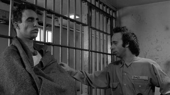 Movie still from “Down by Law” (1986), directed by Jim Jarmusch – A man in a jail cell holding onto a blanket; Medium shot, Over the shoulder angle