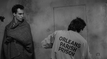 Movie still from “Down by Law” (1986), directed by Jim Jarmusch – A man in a jacket that says orleans parish prison; Medium shot, Over the shoulder angle