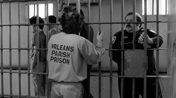 Movie still from “Down by Law” (1986), directed by Jim Jarmusch – A person in a jail cell behind a fence; Medium shot, Over the shoulder angle