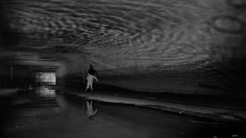 Movie still from “Down by Law” (1986), directed by Jim Jarmusch – A man holding a surfboard while standing in the water; Extreme Wide shot, Low angle