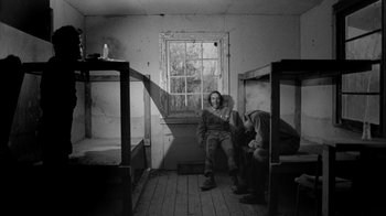 Movie still from “Down by Law” (1986), directed by Jim Jarmusch – A man sitting in a room next to two bunk beds; Wide shot, Over the shoulder angle