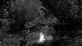 Movie still from “Down by Law” (1986), directed by Jim Jarmusch – A man sitting on the ground near a fire; Medium shot, Low angle