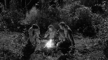 Movie still from “Down by Law” (1986), directed by Jim Jarmusch – A group of people sitting around a fire in the woods; Wide shot, High angle