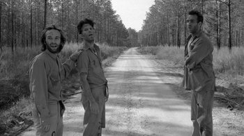 Movie still from “Down by Law” (1986), directed by Jim Jarmusch – A black - and - white photo of three men standing on the side of a road; Medium shot, Low angle