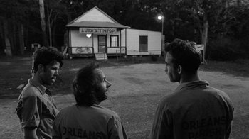 Movie still from “Down by Law” (1986), directed by Jim Jarmusch – A group of men standing in front of a building at night; Medium shot, Over the shoulder angle