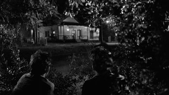 Movie still from “Down by Law” (1986), directed by Jim Jarmusch – Two people sitting in the grass near a tree; Wide shot, Over the shoulder angle