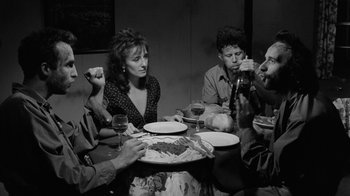 Movie still from “Down by Law” (1986), directed by Jim Jarmusch – A group of people sitting around a table eating food; Medium shot, High angle