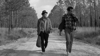 Movie still from “Down by Law” (1986), directed by Jim Jarmusch – Two men walking down a dirt road near a forest; Wide shot, Low angle