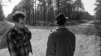 Movie still from “Down by Law” (1986), directed by Jim Jarmusch – Two people standing in front of a wooded area; Medium shot, Over the shoulder angle