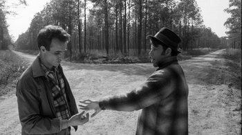 Movie still from “Down by Law” (1986), directed by Jim Jarmusch – Two men in a wooded area one of which is holding something in his hand and the other is holding something in his other hand; Medium shot, Over the shoulder angle