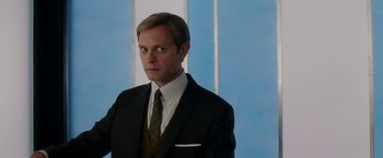 Movie still from “Down with Love” (2003), directed by Peyton Reed – A man wearing a suit and tie standing in front of a blue wall; Close Up shot, Over the shoulder angle