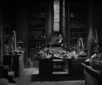 Movie still from “Dr. Jekyll and Mr. Hyde” (1931), directed by Rouben Mamoulian – A man sitting at a desk in a room filled with lots of stuff; Wide shot, High angle