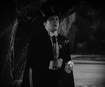 Movie still from “Dr. Jekyll and Mr. Hyde” (1931), directed by Rouben Mamoulian – A man wearing a top hat and a long black coat standing next to a tree; Medium shot, Low angle