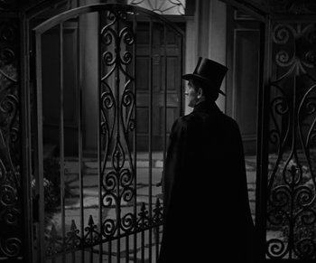 Movie still from “Dr. Jekyll and Mr. Hyde” (1931), directed by Rouben Mamoulian – A man wearing a top hat and a long coat standing in front of an iron gate; Medium shot, Over the shoulder angle