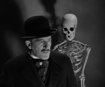 Movie still from “Dr. Jekyll and Mr. Hyde” (1931), directed by Rouben Mamoulian – A man wearing a top hat standing in front of a skeleton; Medium shot, Low angle