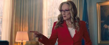 Movie still from “Don't Look Up” (2021), directed by Adam McKay – A woman in a red suit points to something in her hand; Medium shot, Low angle