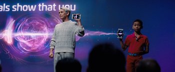 Movie still from “Don't Look Up” (2021), directed by Adam McKay – A man holding up a cell phone while standing on a stage; Medium shot, Over the shoulder angle