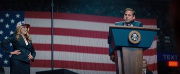 Movie still from “Don't Look Up” (2021), directed by Adam McKay – A man standing at a podium in front of an american flag; Medium shot, Low angle