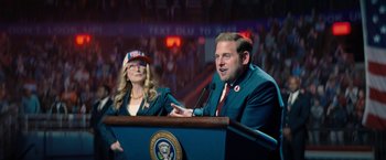 Movie still from “Don't Look Up” (2021), directed by Adam McKay – A man and a woman are speaking at a podium in front of an audience; Medium shot, Over the shoulder angle
