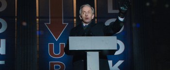 Movie still from “Don't Look Up” (2021), directed by Adam McKay – A man in a black jacket is speaking at a podium; Medium shot, Low angle
