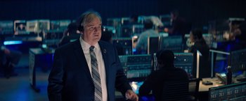 Movie still from “Don't Look Up” (2021), directed by Adam McKay – A man wearing a suit and tie in a room with a bunch of people; Medium shot, Over the shoulder angle