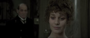 Movie still from “Dracula” (1979), directed by John Badham – A young woman with a curly hair style looking at the camera with a man in the background; Close Up shot, Over the shoulder angle