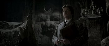 Movie still from “Dracula” (1979), directed by John Badham – A man in a suit holding a book in a dark room; Medium shot, Low angle