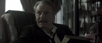 Movie still from “Dracula” (1979), directed by John Badham – An older man sitting in a chair with a book in his hand; Close Up shot, Low angle