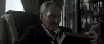 Movie still from “Dracula” (1979), directed by John Badham – An older man sitting in a chair reading a book; Close Up shot, Low angle