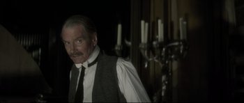 Movie still from “Dracula” (1979), directed by John Badham – An older man in a vest and tie standing in front of candles; Medium shot, Over the shoulder angle