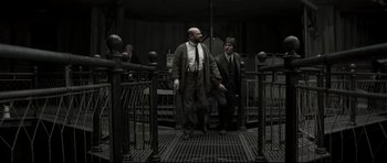 Movie still from “Dracula” (1979), directed by John Badham – Two men in suits and ties walking through a metal fence; Wide shot, High angle